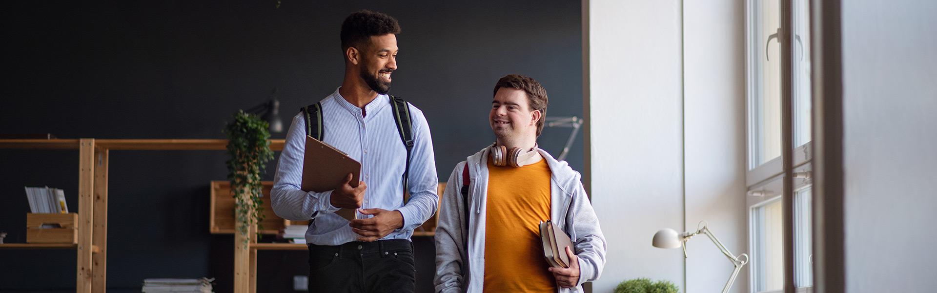 young man with down syndrome holding a book and walking along side a mentor