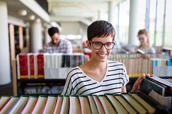 a young student with a pixie hair cut and glasses is standing in front of books on a shelf