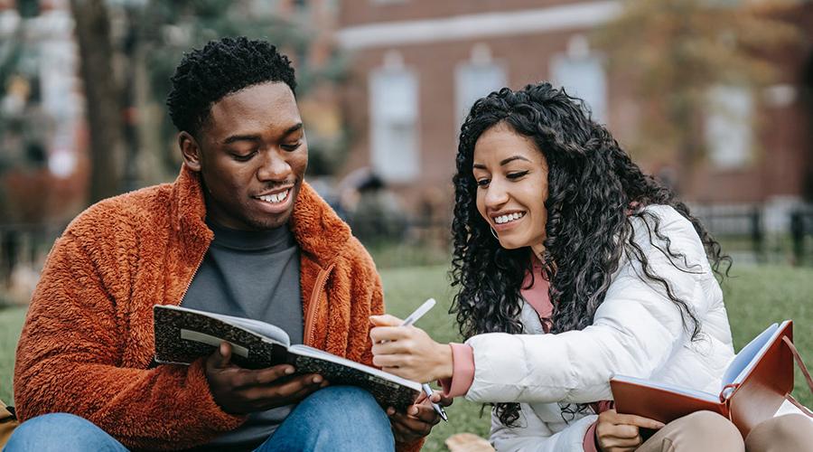 a male and female student writing in notebooks on campus